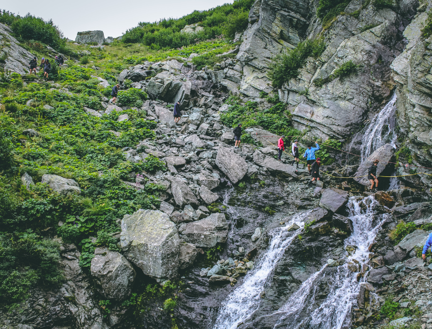 A group of hikers tackling rugged terrain near a cascading waterfall, showcasing the thrill of waterfall walks in North Wales.