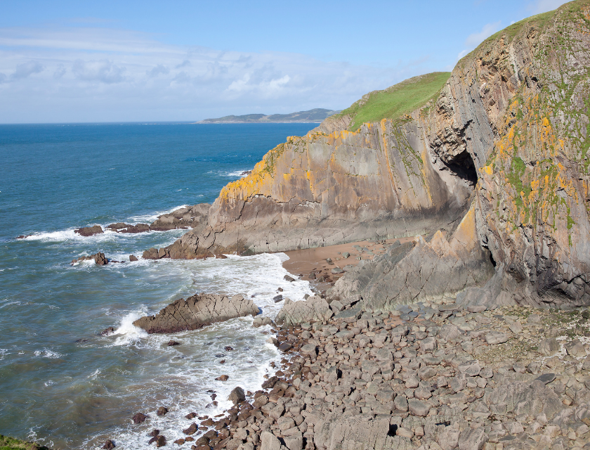 Rocky cliffs at Baggy Point, Croyde.  Waves crash against the rocks below, with a small hidden beach tucked away at the base of the cliff.