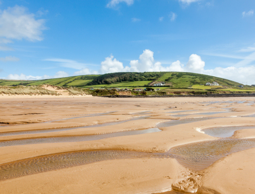 Rolling hills and gentle waves at Croyde Beach, ideal for families to explore or relax. The sun shines brightly, highlighting the stunning North Devon coastline.