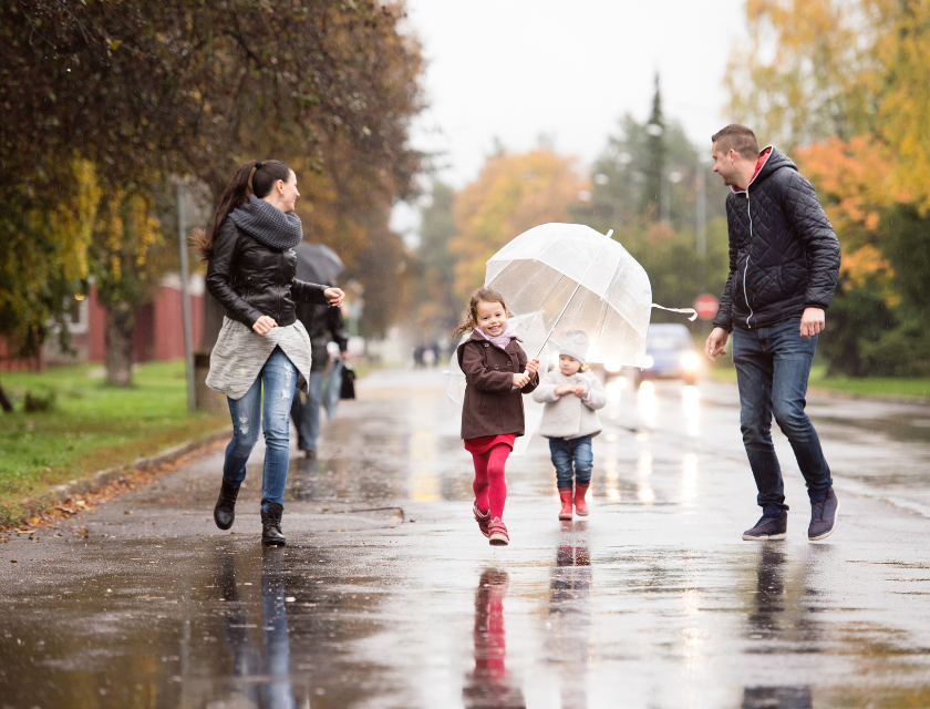 A  father, mother and two children walking and smiling in the rain with umbrellas.