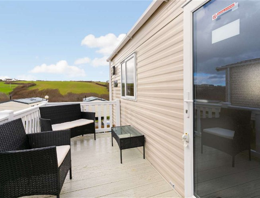 A seating area on the decking of a static caravan, looking out over green hills.