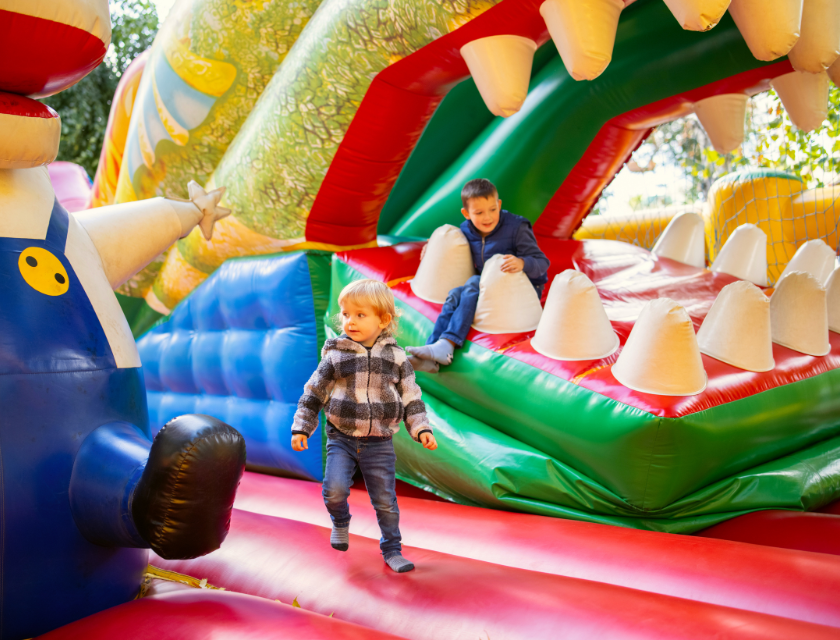 Children playing in a colorful inflatable play area shaped like a dinosaur's mouth –