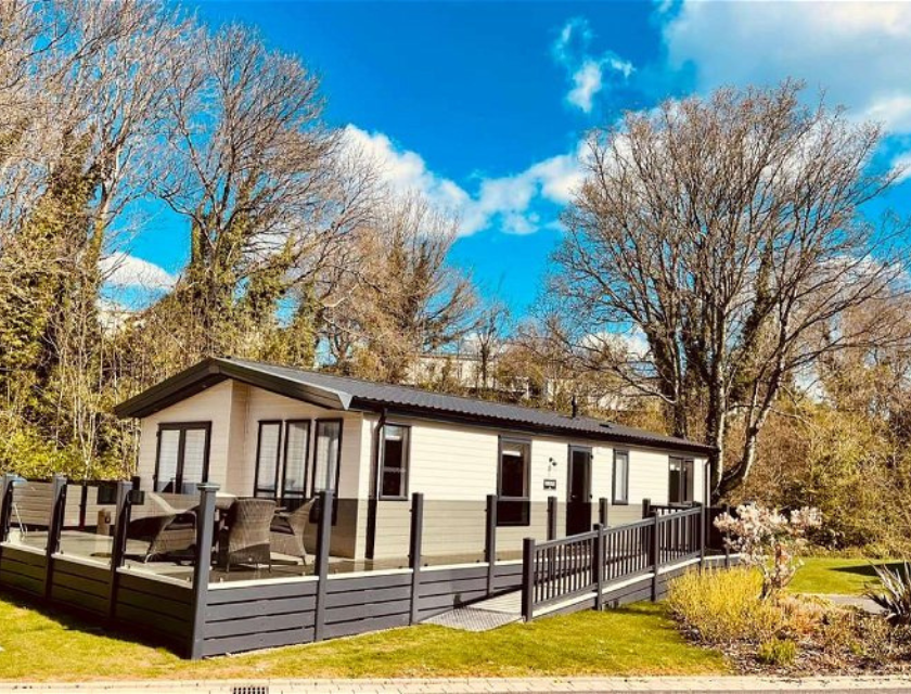 A contemporary static caravan with a spacious wooden deck, nestled among trees in a quiet  dog-friendly caravan park in Devon.