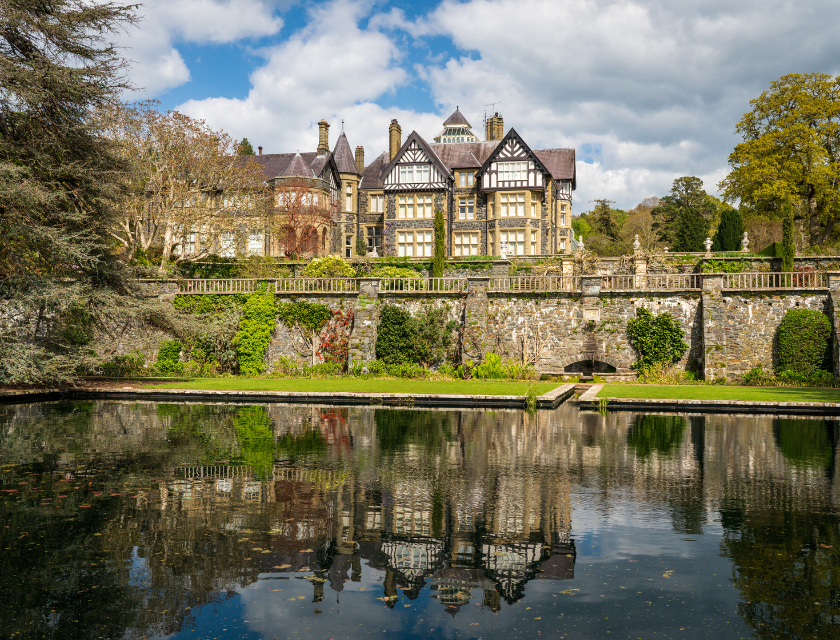 The beautiful mansion at Bodnant Garden in Conwy, North Wales, reflected in a pond, surrounded by greenery and landscaped gardens