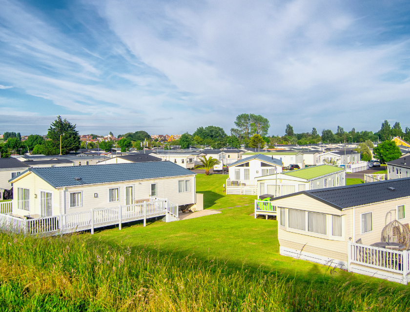 Rows of white static caravan homes with small verandas are set in a grassy holiday park on a sunny day. A stay at a caravan park is the ideal base to try the dog-friendly activities in Cornwall.