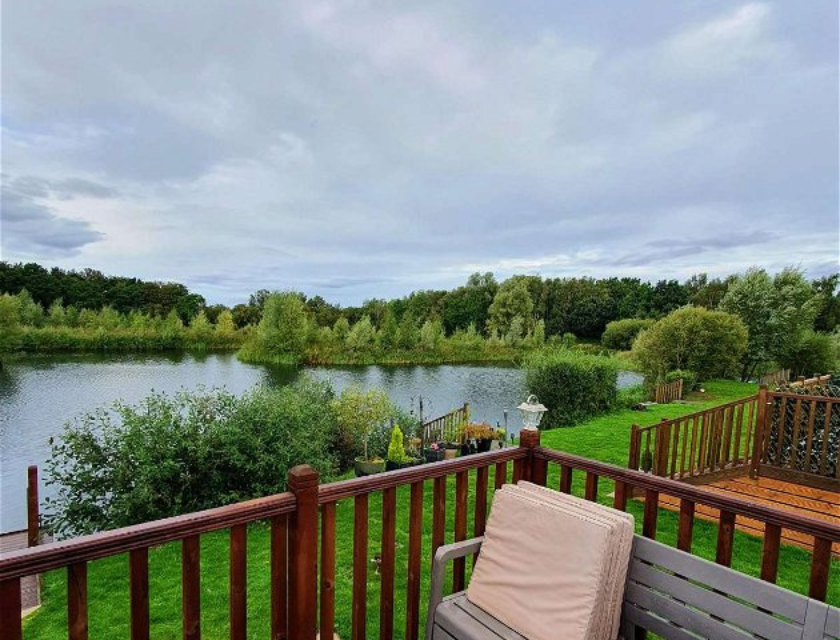 Peaceful lake surrounded by trees, viewed from a wooden deck with outdoor seating.