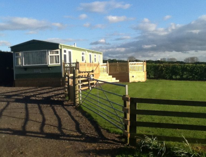 Static caravan in the countryside with a fenced garden, under a bright blue sky