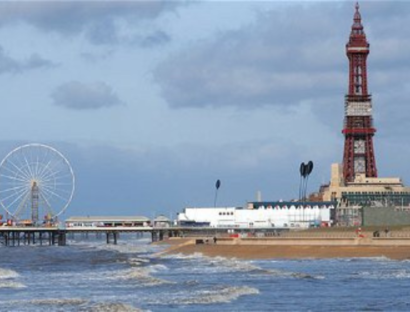 Wide shot of Blackpool beach with it's tower and pier under a bright sky.