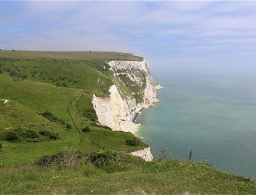 White Cliffs of Dover rising above the sea with grassy hills and a walking trail. Stay in the south or south east of England for close access to some of the best autumn walks in the uk.