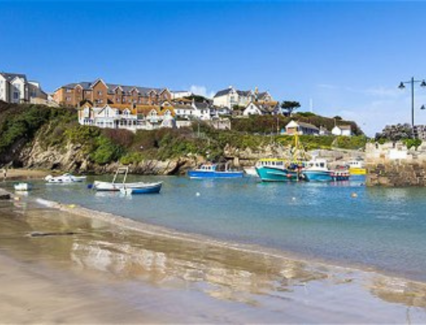 Sandy beach in a seaside village, with fishing boats and houses in the background. Home to the South West Coastal Path, you can find some of the most peaceful autumn walk in the UK in Cornwall.