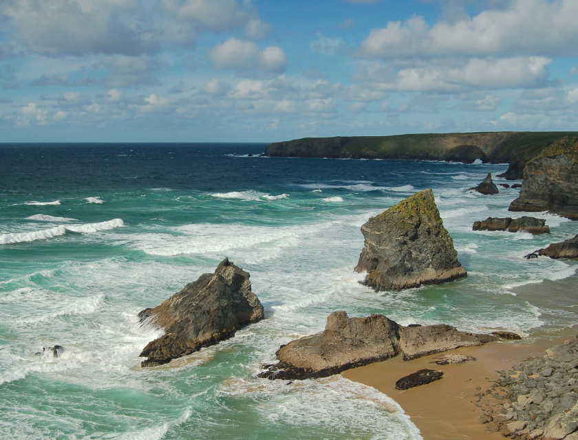 Rocky cliffs on the coast with waves crashing against them under a cloudy sky. Home to the South West Coastal Path & popular autumn walks in the uk