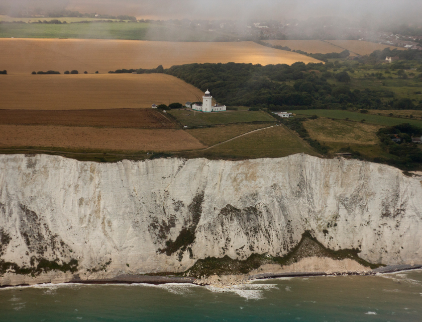 White Cliffs of Dover with a lighthouse overlooking the sea, and farmland visible.