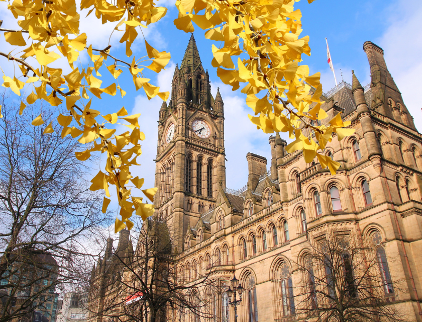 Manchester’s Town Hall in autumn, framed by golden leaves against a bright blue sky.