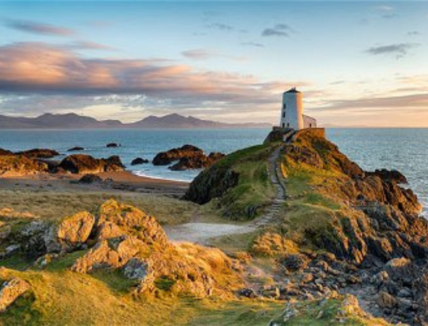 Lighthouse on rocky cliffs with a sea view and mountains in the background.