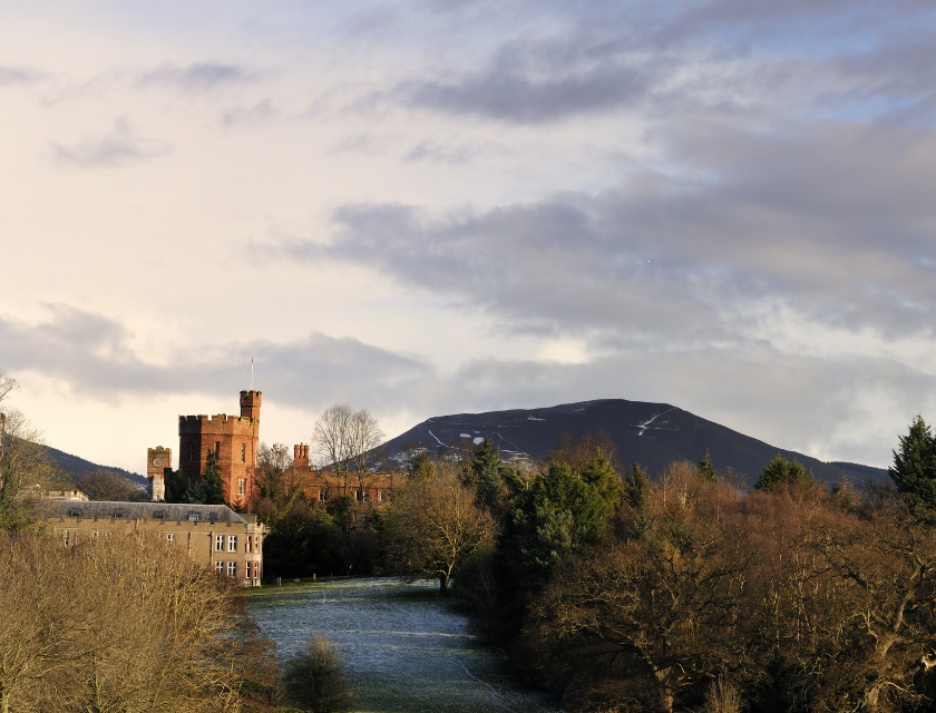 Castle with red-brick towers & backdrop of misty hills. The sky is slightly overcast