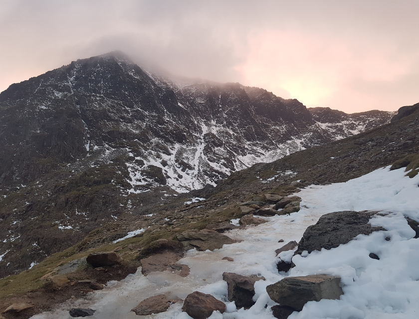 Snow-capped mountain path in Snowdonia National Park. With clouds and mist around the peaks.