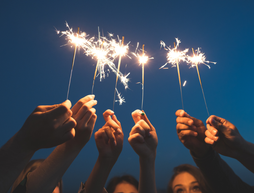 A group of people holding sparklers together against a dark blue sky, creating a festive New Year's Eve celebration scene.