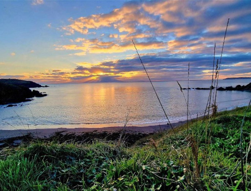 Sunset over a calm beach with clouds reflecting on the water.