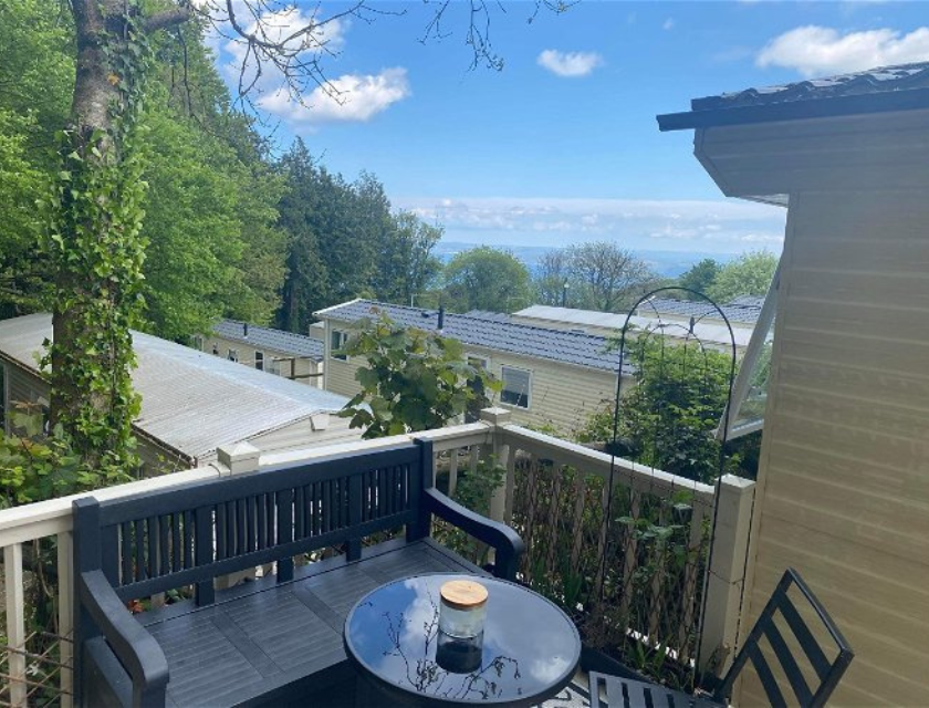 Static caravan deck with seating area overlooking a group of caravans and distant sea view