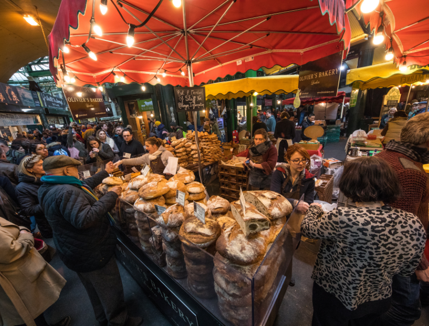 A busy bakery stall at a market with customers buying fresh bread.