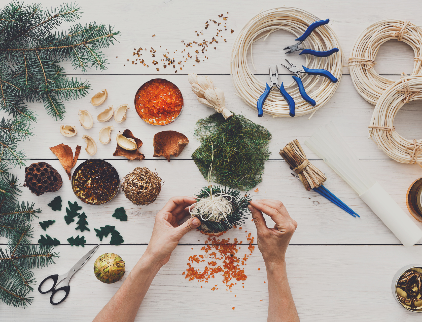 A person making Christmas crafts using pine cones, wreaths, and sparkly decorations. There are opportunities for crafts at Christmas markets in Lincolnshire.