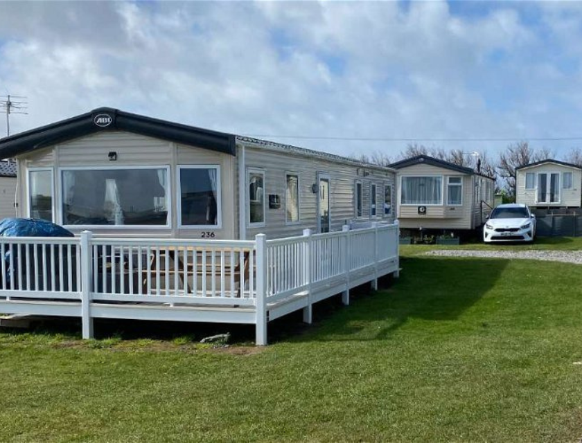 Static holiday caravan at Harlyn Sands, Cornwall with a white railing around its deck, parked on a grassy area at a holiday park. A perfect base to visit Christmas markets in Cornwall.