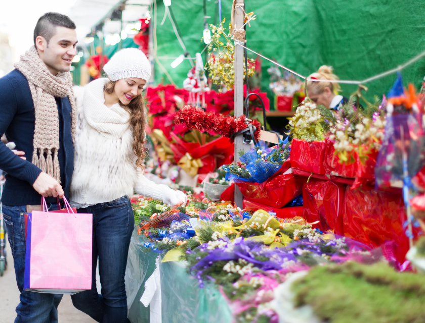 Couple in winter clothes enjoying a Christmas market, looking at flowers and festive decorations.