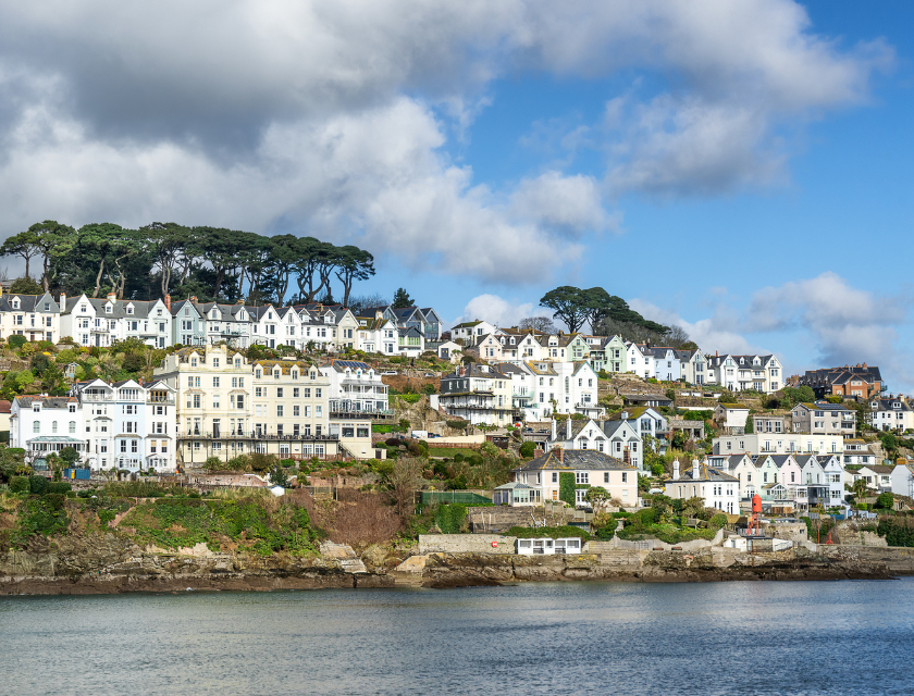 Town of Fowey, with white houses on a hill, overlooking the water on a bright, cloudy day.