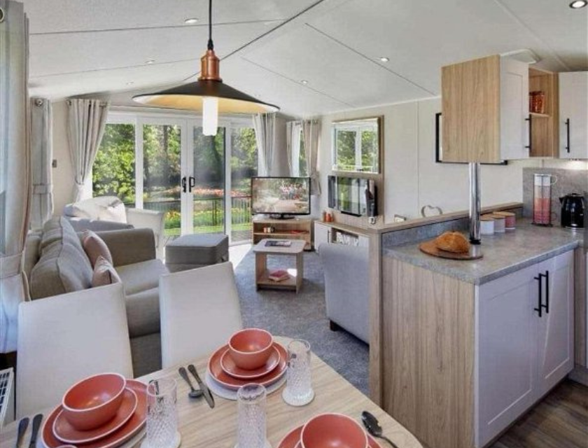 Living room and kitchen inside a static caravan holiday home with seating, a TV, and a bright dining area overlooking a garden through large patio doors.. An ideal base for your visits to Cornwall's Christmas markets.