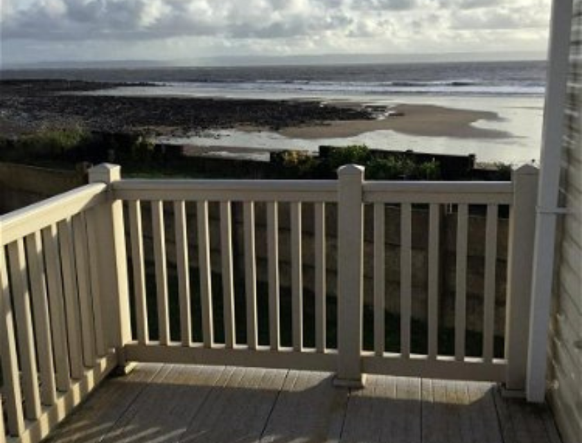 A view from a static caravan deck overlooking a peaceful beach with a cloudy sky above. A perfect spot for October half term caravan breaks.