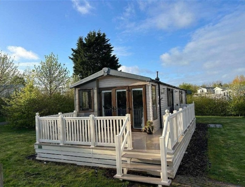 Static caravan with white railings surrounded by greenery and blue skies. Ideal for October half term caravan breaks with the family.