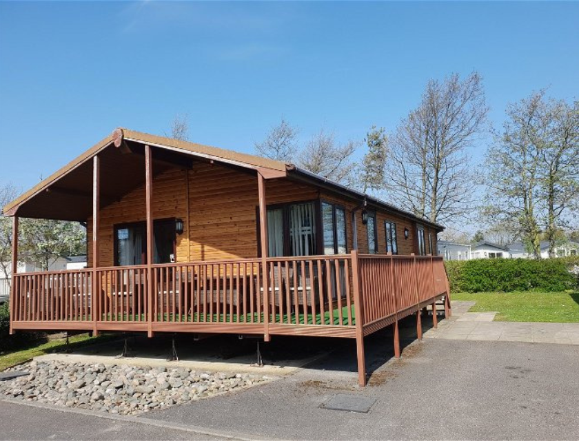 Wooden holiday lodge with a raised deck and green grass. A perfect location for your Haven Christmas break.