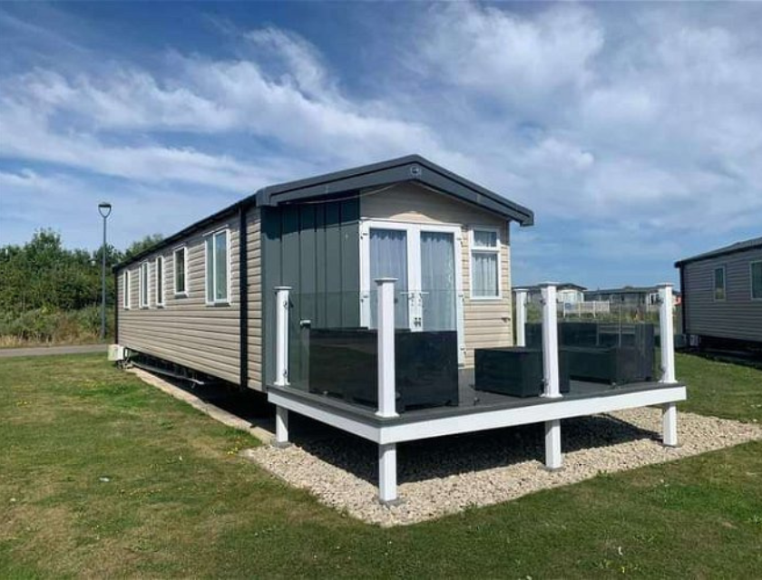 Enjoy your Haven Christmas break in comfort. Static caravan holiday home with a modern style decking and glass railing, on a green park under a blue sky.