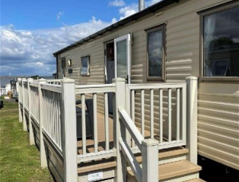 Beige static caravan with white railings and a front deck, set on a grassy holiday park under a cloudy sky. A perfect escape for your Haven Christmas breaks.