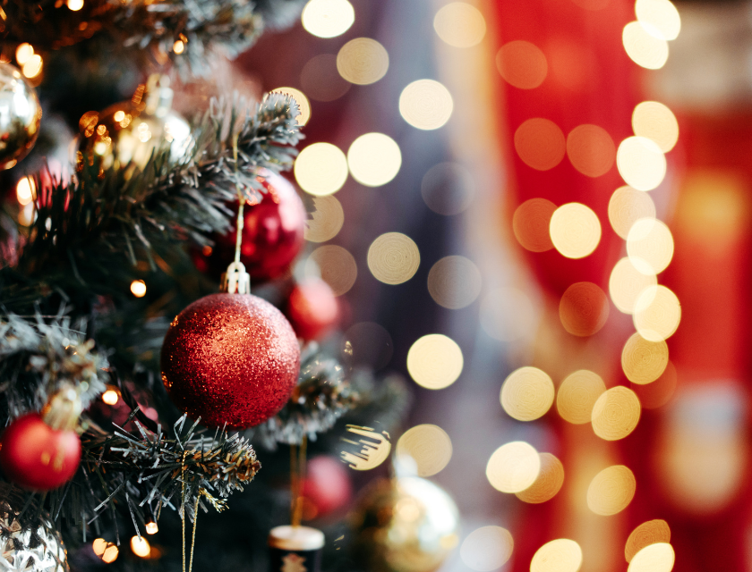 A close-up of a sparkling Christmas tree decorated with red and gold baubles, with warm, glowing lights in the background.