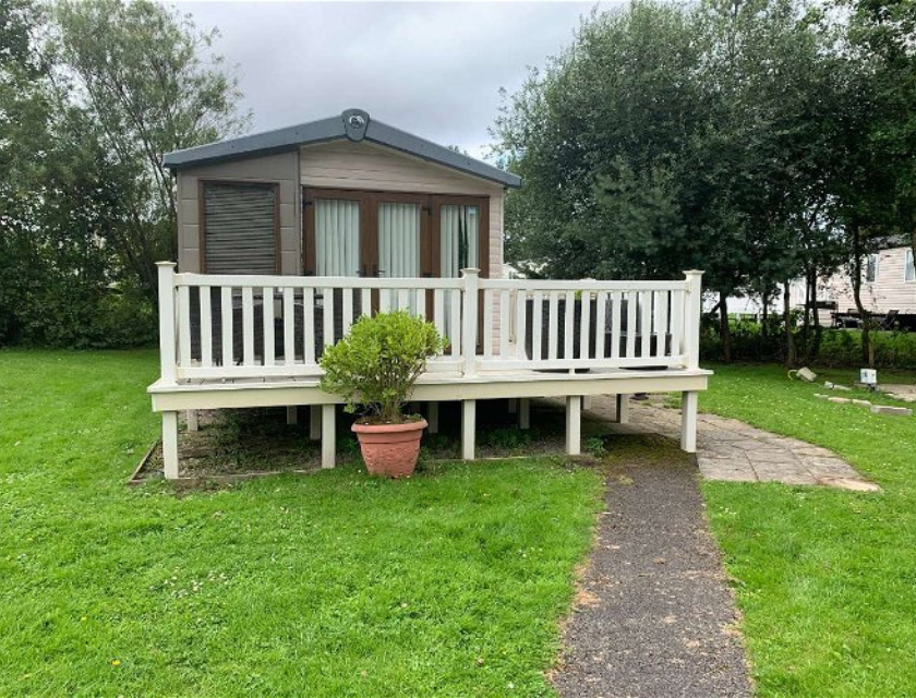 Static caravan with a white decking, surrounded by green grass. A perfect spot for quiet UK autumn activities.