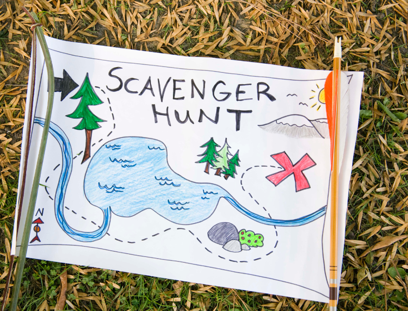 Hand-drawn map for a scavenger hunt lying on the grass. The map shows a river, trees, and a big red "X" marking the treasure, with arrows leading the way.