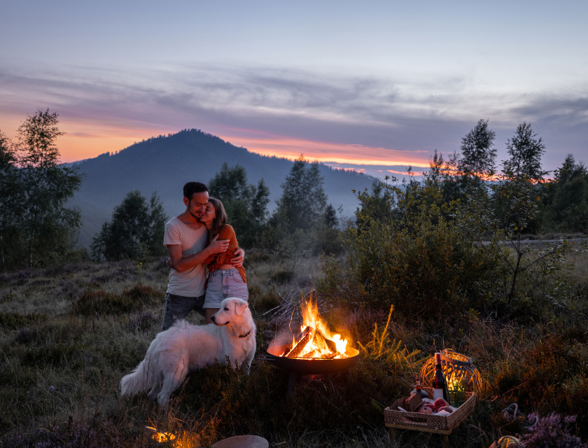 Couple hugging by a campfire with their golden retriever on a evening glamping trip.